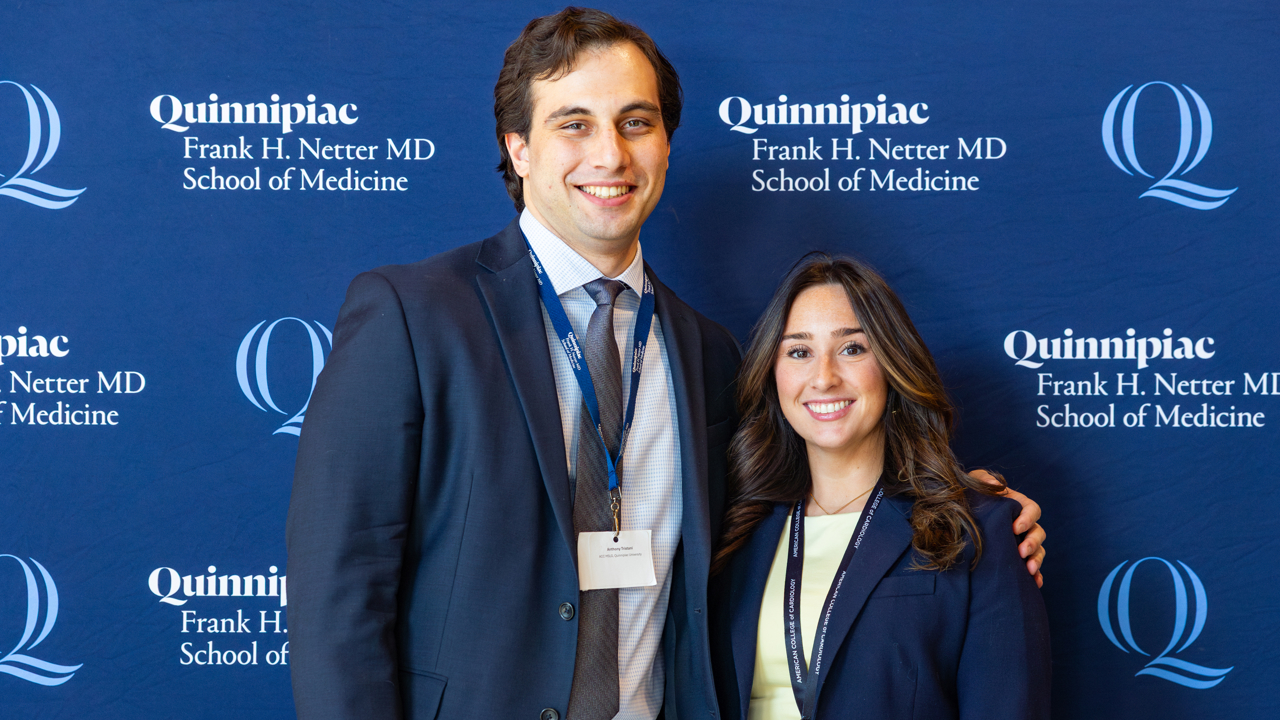 Two students pose in front of a Quinnipiac backdrop.