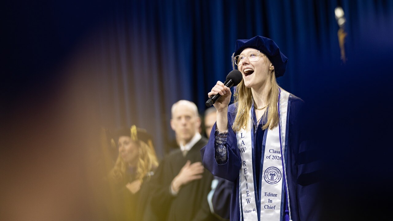 Olivia Ventura in graduation robes holds microphone and sings