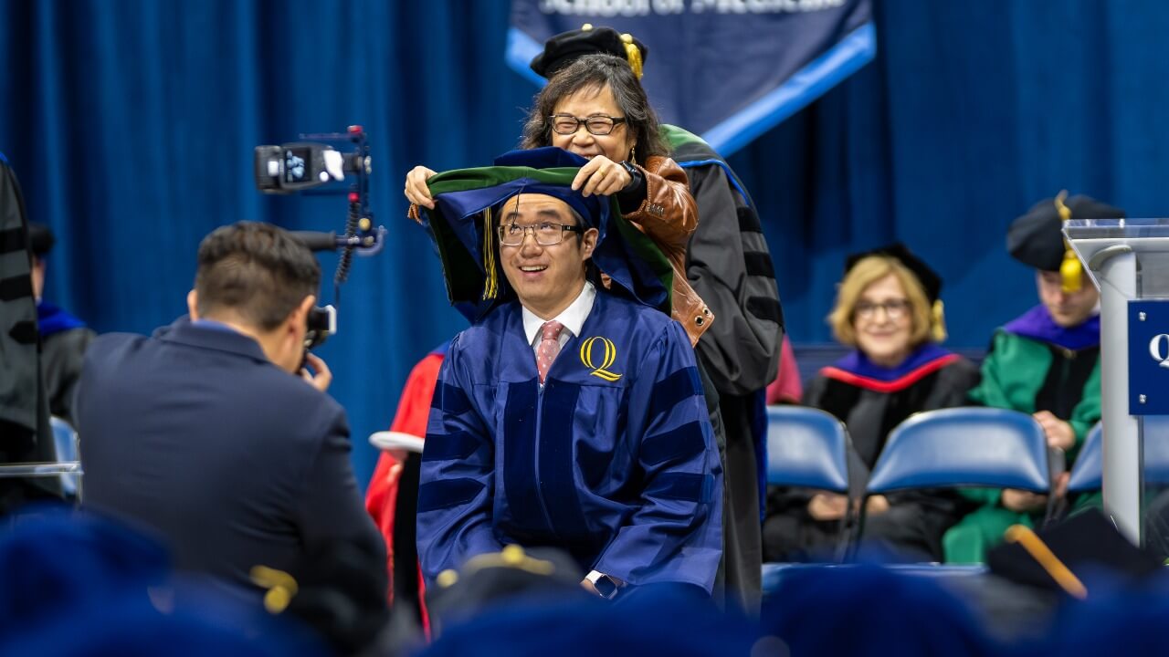 Graduate receives their hood from a loved one on stage