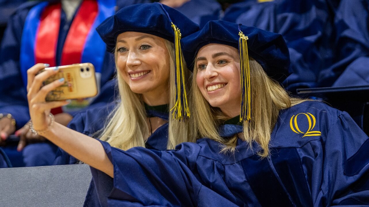 Two graduates smile and take a selfie