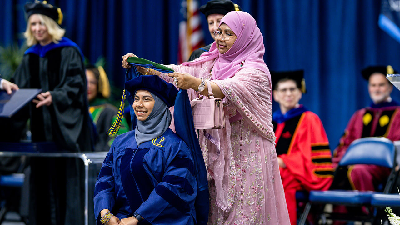 Graduate being hooded by accompanying guest on graduate stage