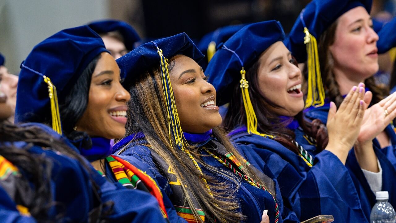Three graduates smile and clap at Commencement