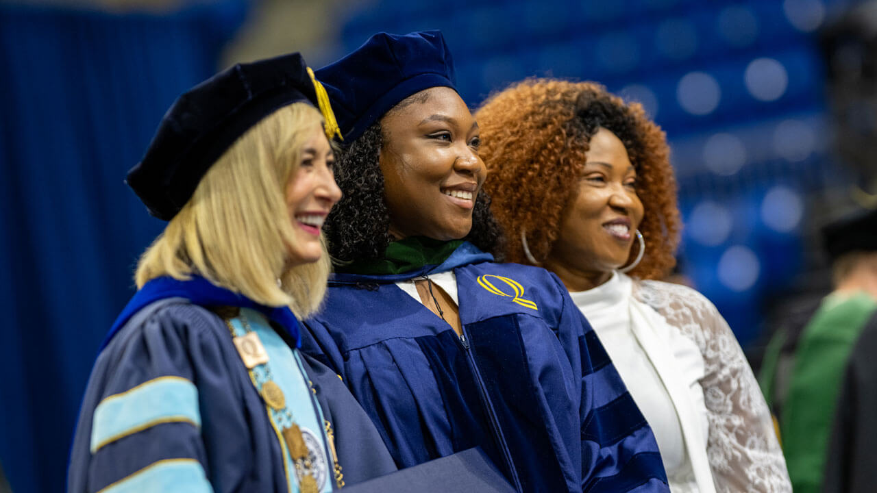 President Marie Hardin smiles alongside a 2026 School of Medicine graduate and her loved one on stage