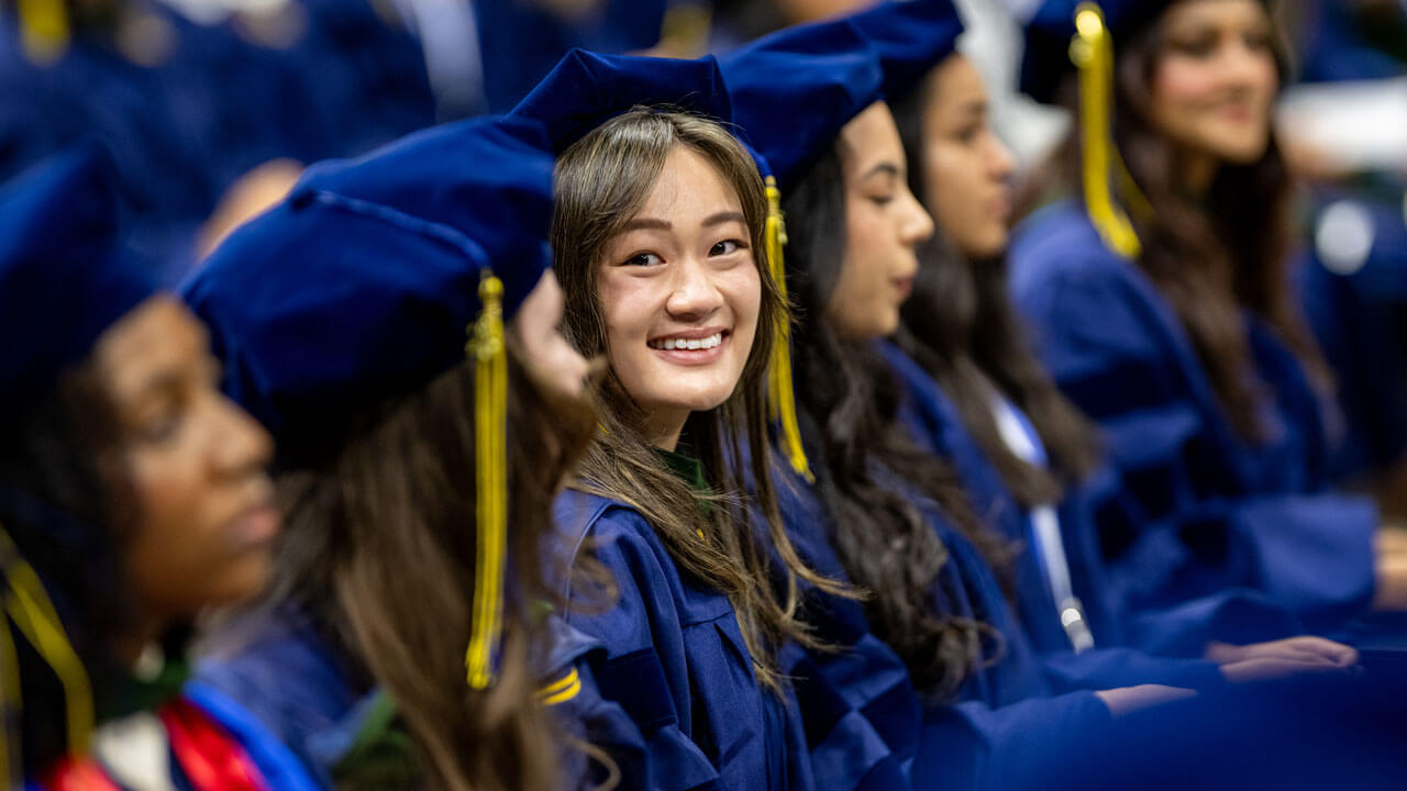 Class of 2026 School of Medicine graduate smiles with her cap and gown while sitting down