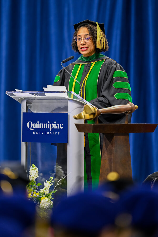 Monique Nugent speaks behind a podium with the Commencement mace in the foreground