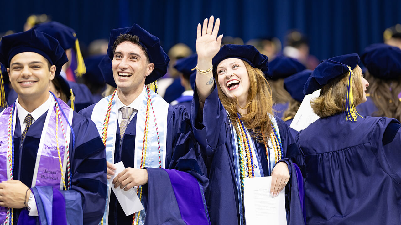 Graduates stand together and wave to people above them