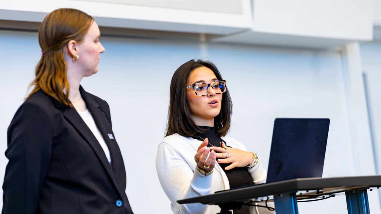 Students stand at a podium presenting their work.