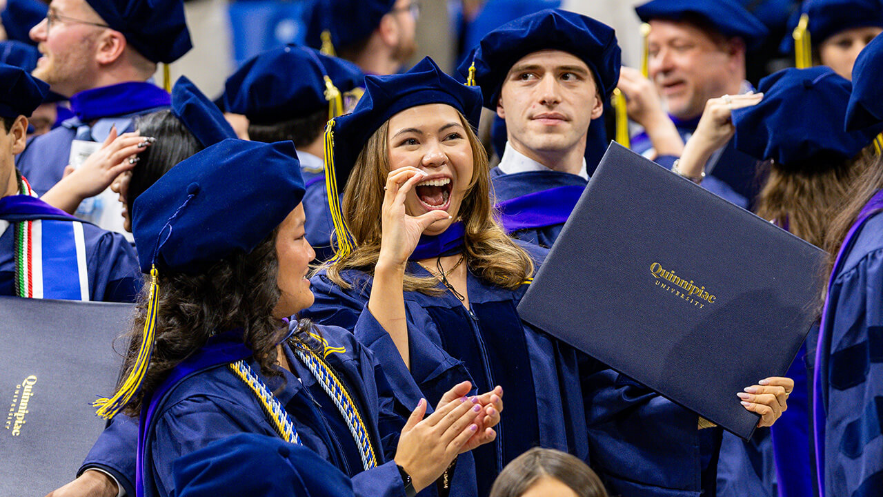 Graduate makes a heart with their hand while holding up diploma