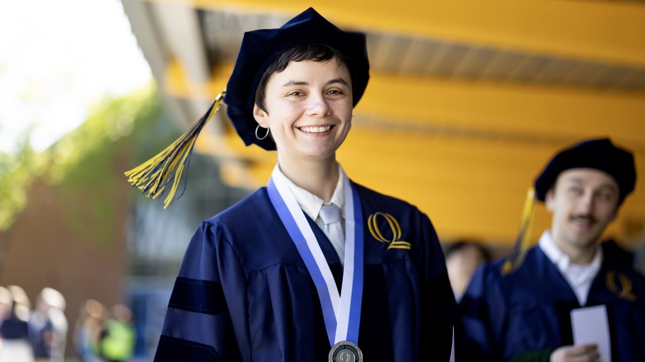 Graduate in cap and gown smiles at camera.