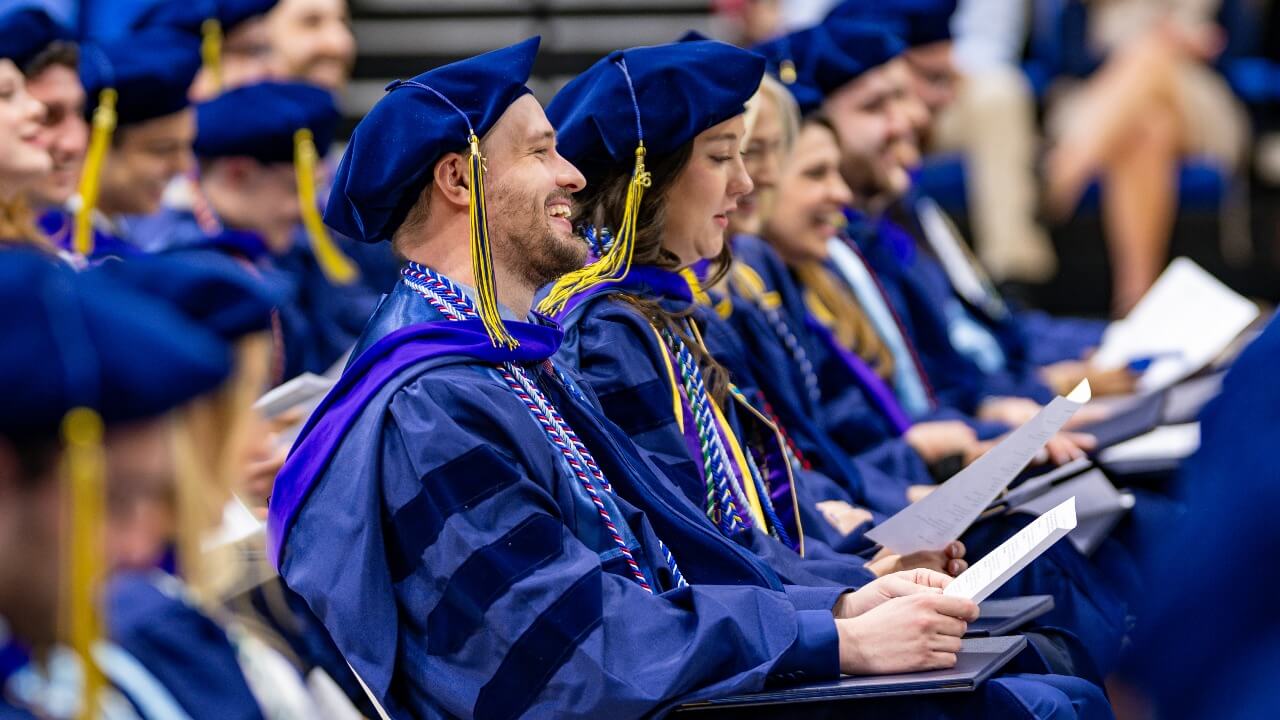 Graudates sit next to each other in the audience of the ceremony