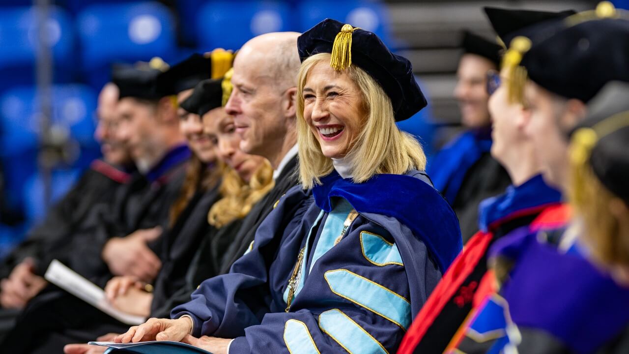 President Marie Hardin sitting on the stage and smiling at the graduates
