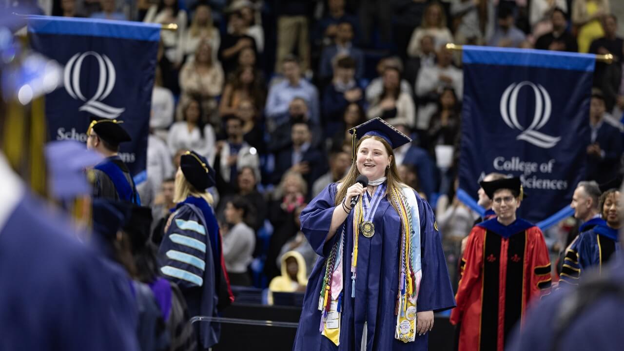 Graduate in cap and gown sings on stage.