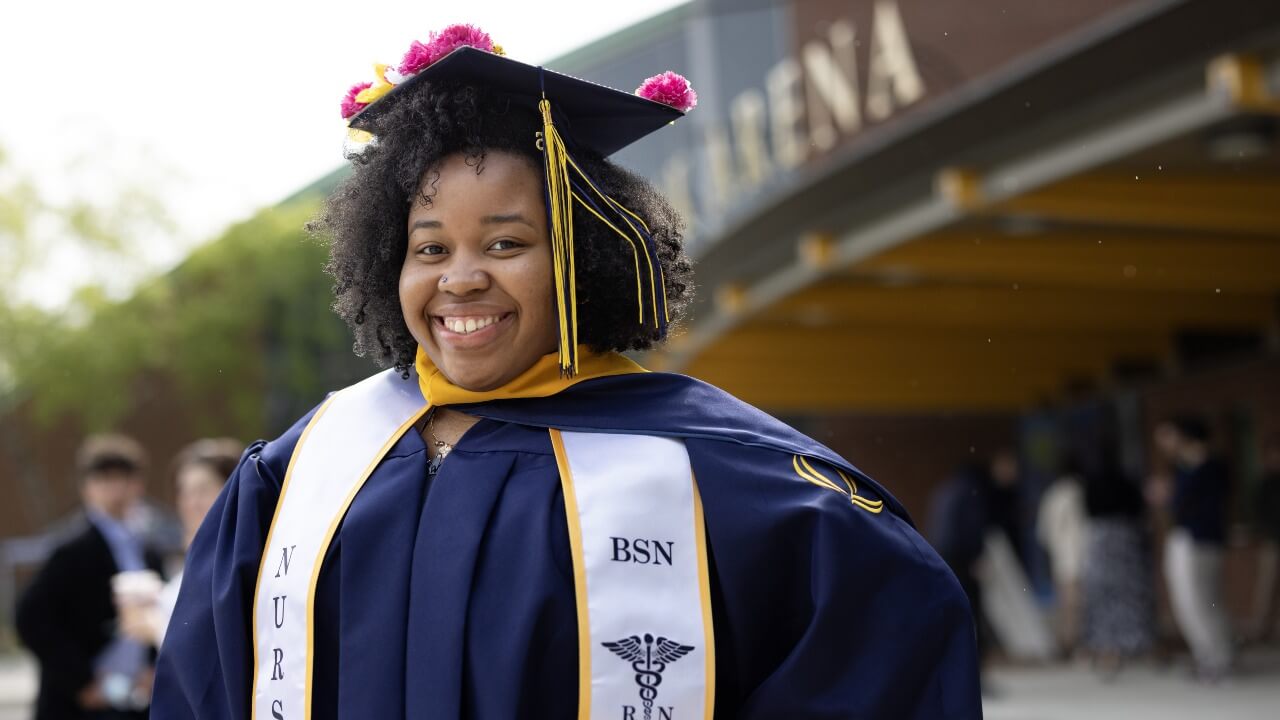 Graduate in cap and gown smiles at the camera.