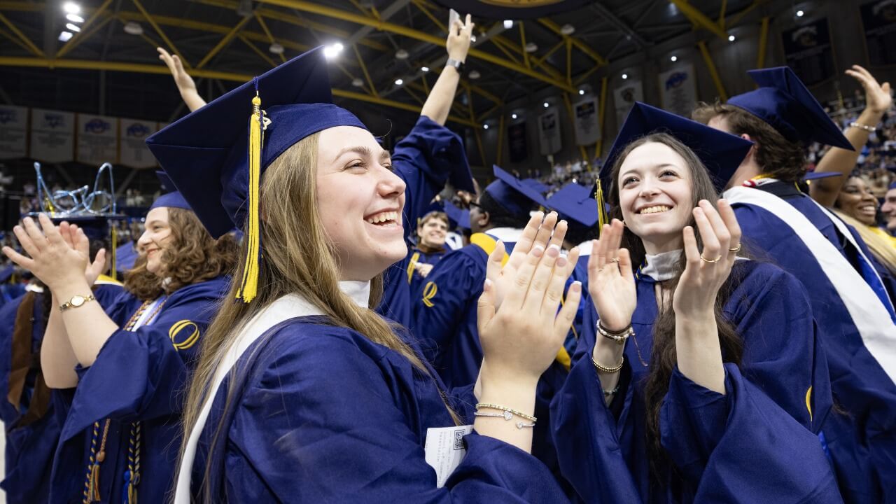 Graduates in caps and gowns clap.