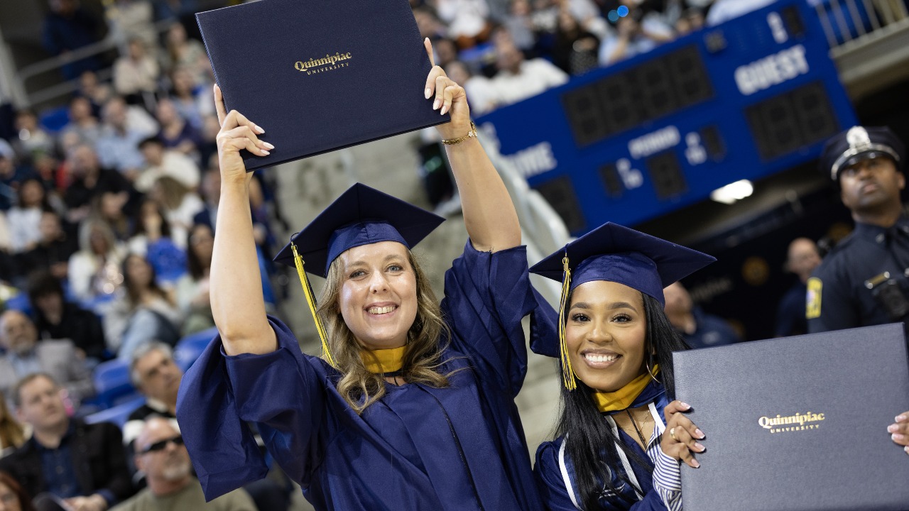 Two graduated hold up their diplomas and smile