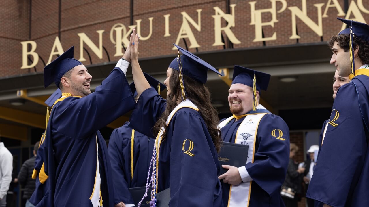 Graduate students high-fiving and smiling at Commencement