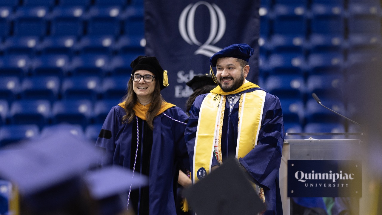 A graduate stands on stage and looks out at the crowd