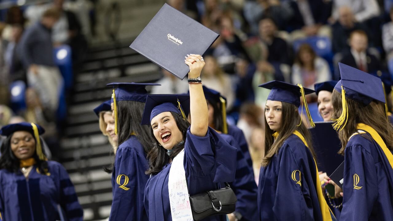 Graduate holds up diploma as they walk out of arena following commencement ceremony