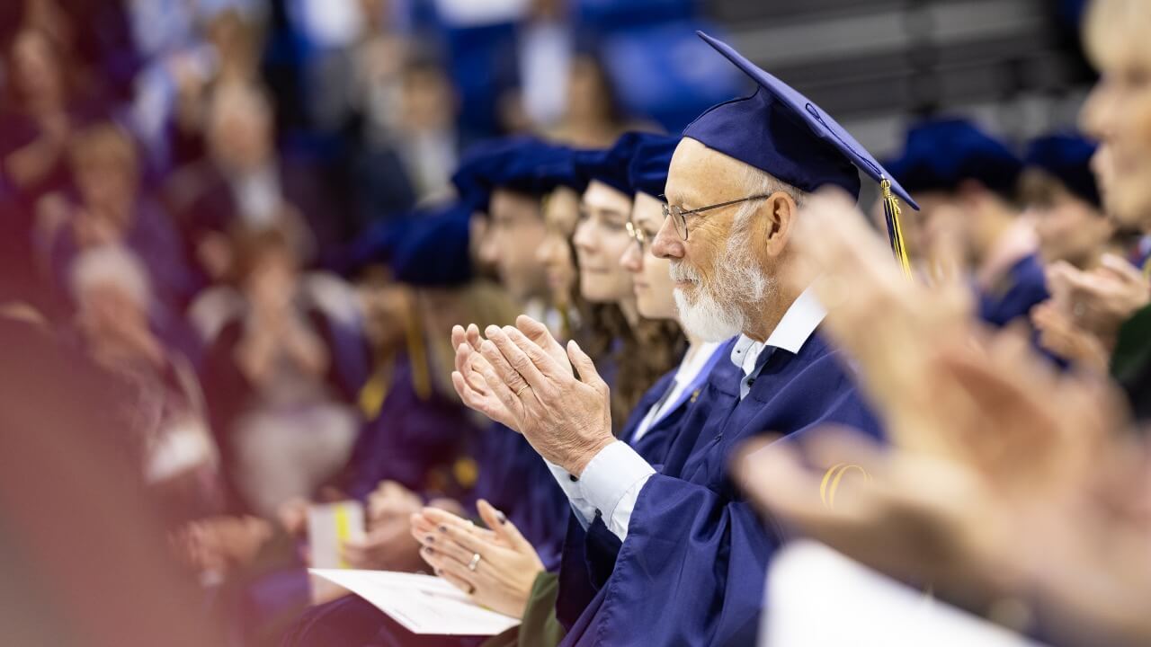 Graduate in cap and gown claps at Commencement