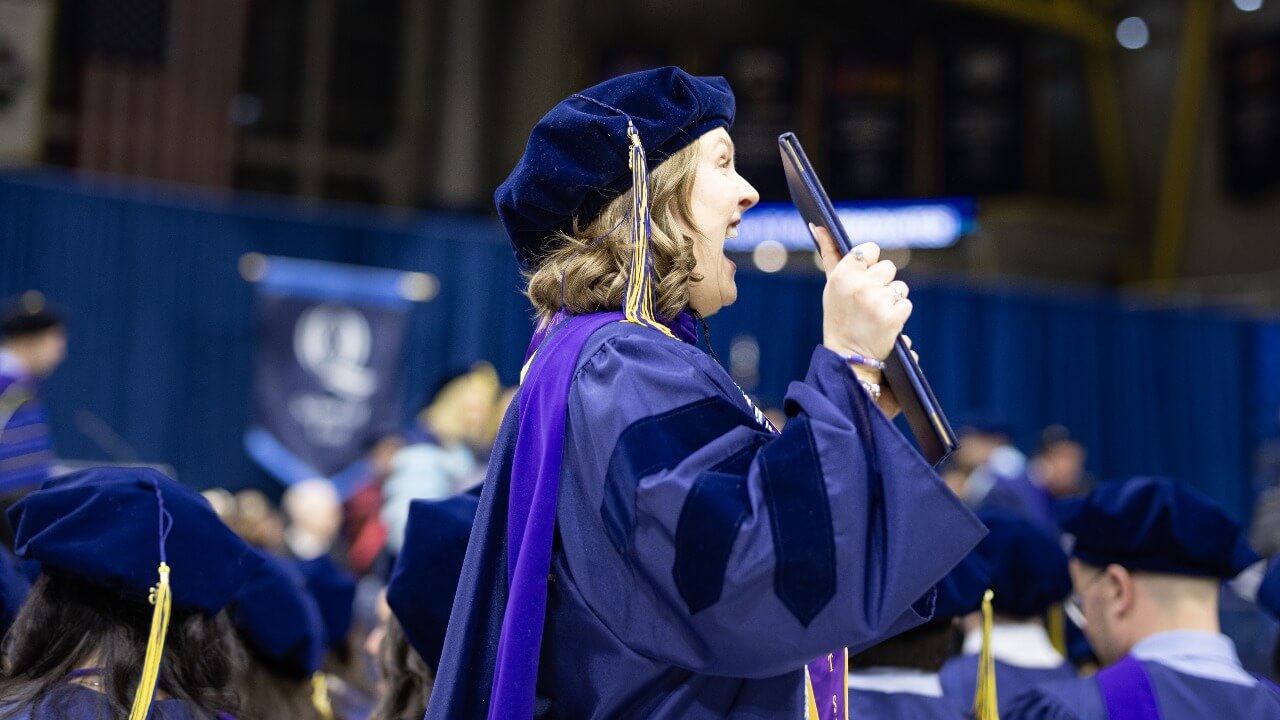 Graduate in cap and gown cheers while holding their diploma.