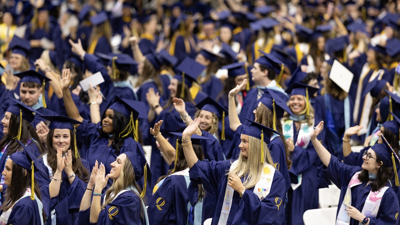 Graduates wave as they wait to walk the stage at commencement