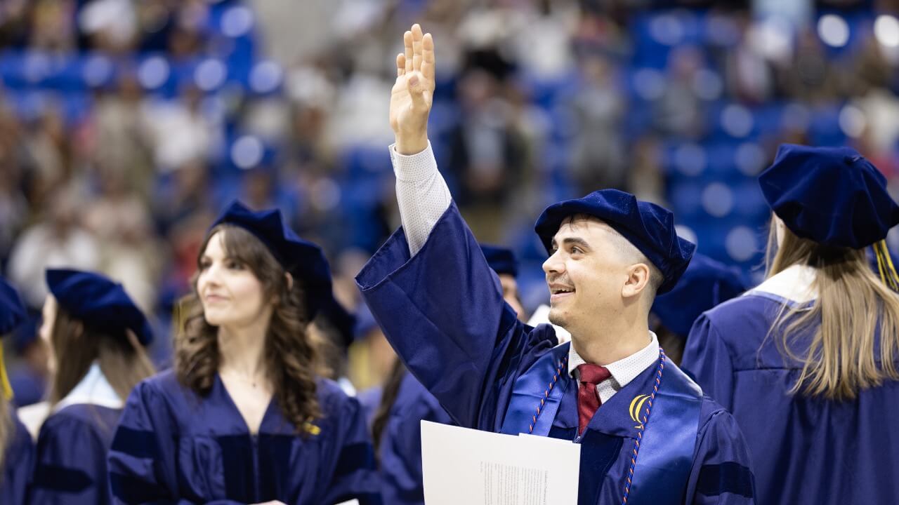 Graduate raises hand and smiles at Commencement