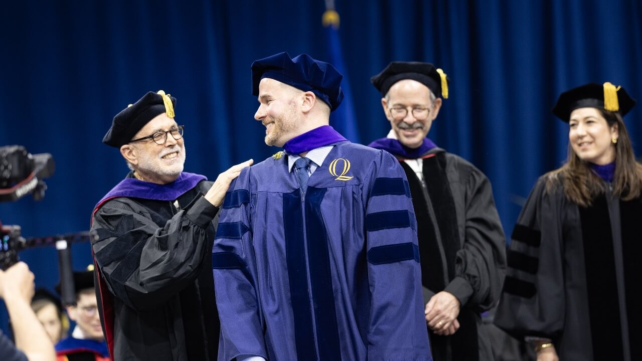 Professor John Thomas and graduate smile at eachother while being hooded