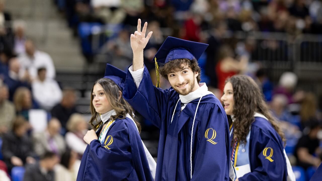 Graduate holds up peace sign while walking into Commencement