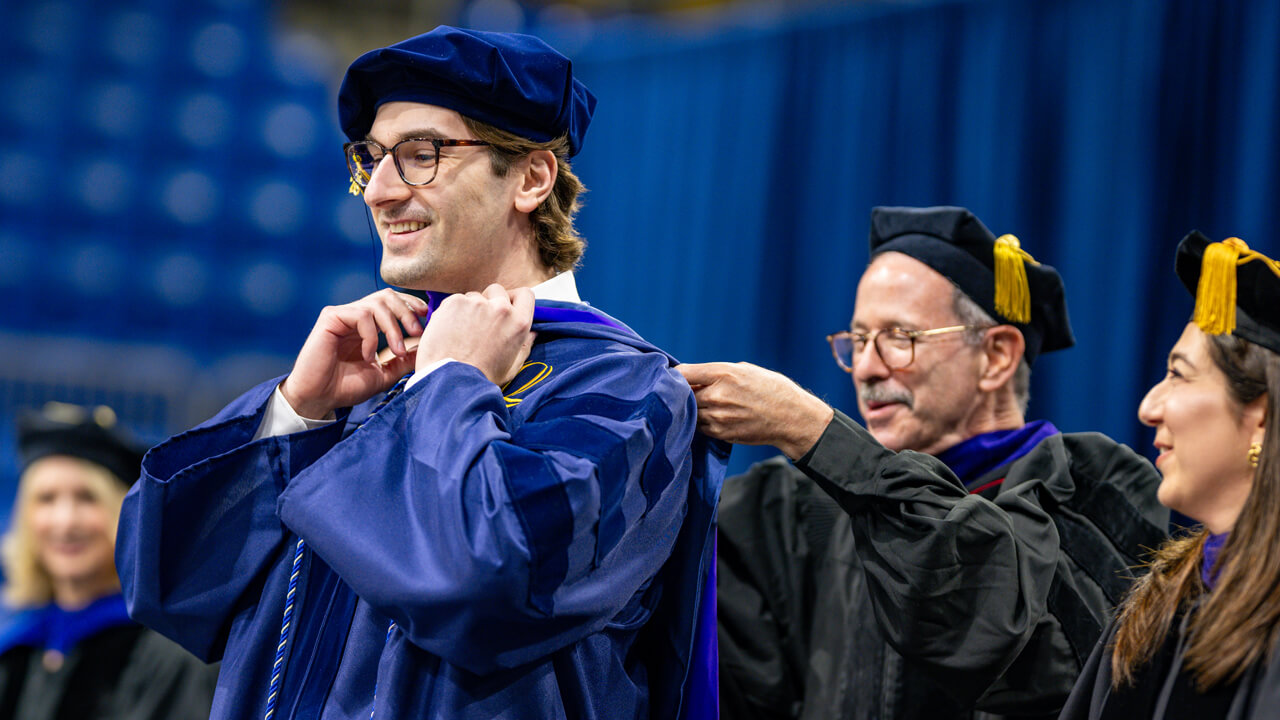 A graduate receives his doctoral hood from professors on stage