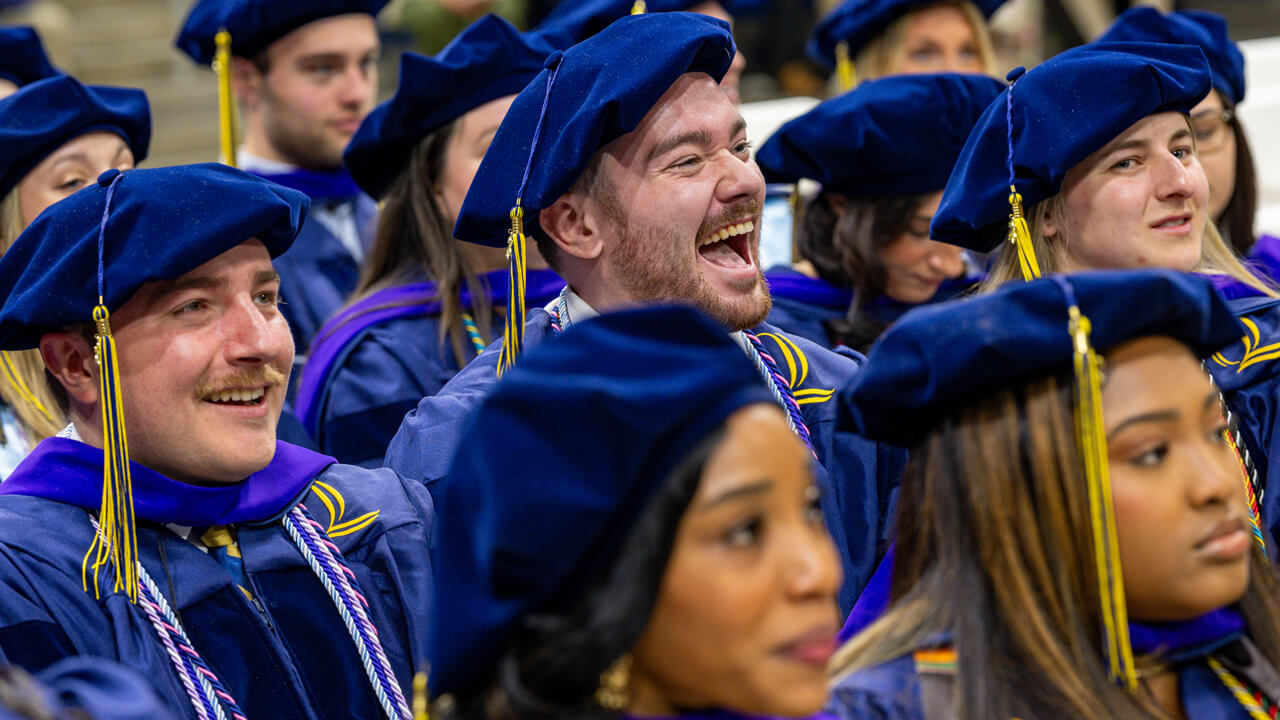 Graduates seated in a row cheer and smile