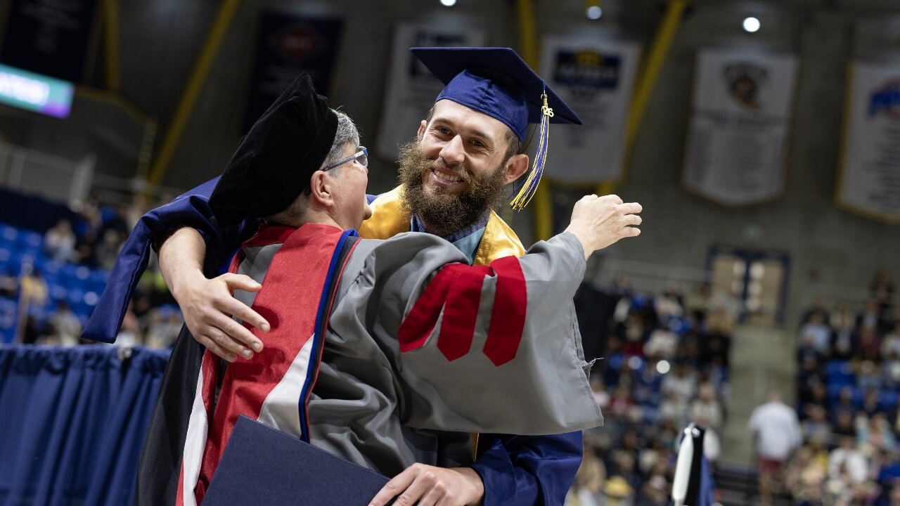 Graduate and faculty member hugging in their regalia