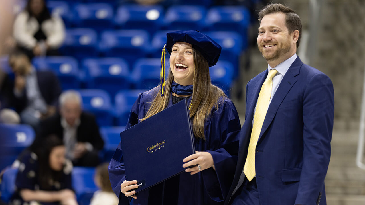Graduate stands with guest and holds degree as they smile together