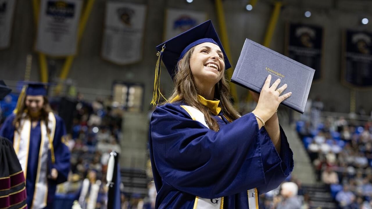 Graduate holding up their diploma next to their head and smiling