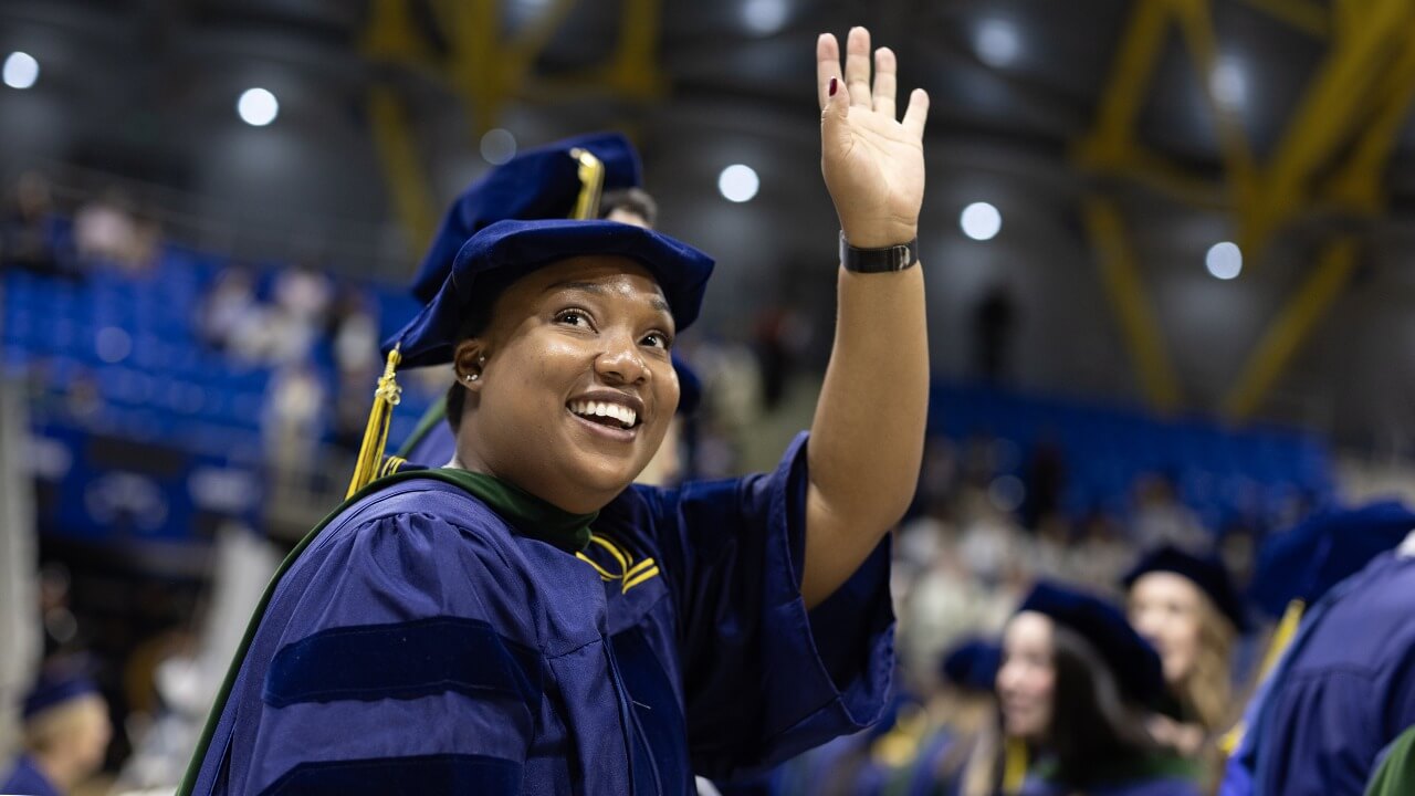 Graduate in cap and gown raises hand.