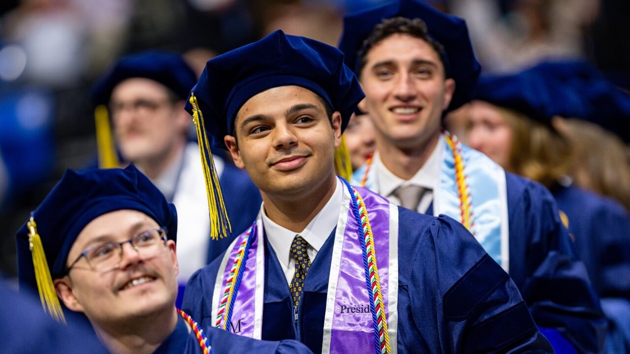 Three graduates smile as they stand at Commencement