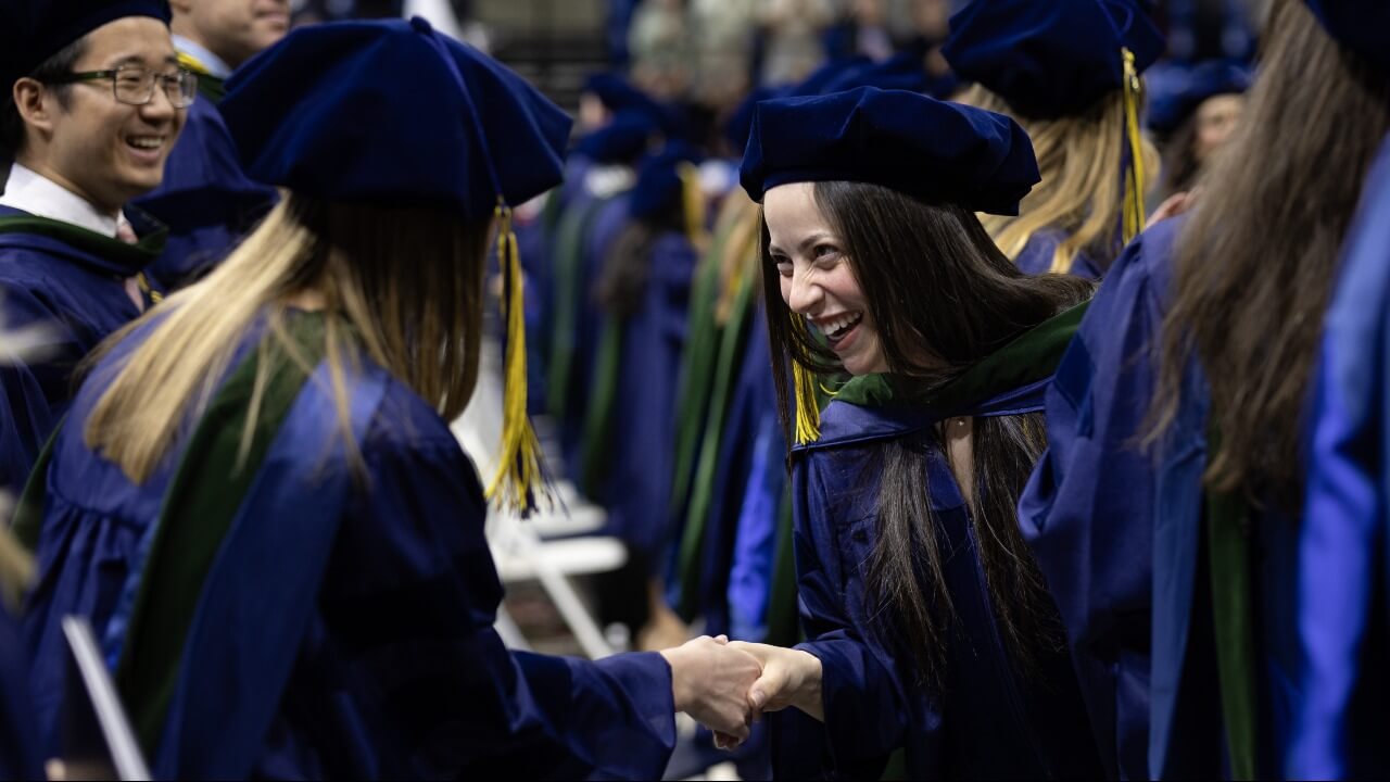 Graduates shake hands in cap in gown.