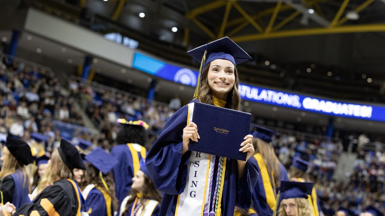 Graduate holding their diploma in front of their chest and smiling