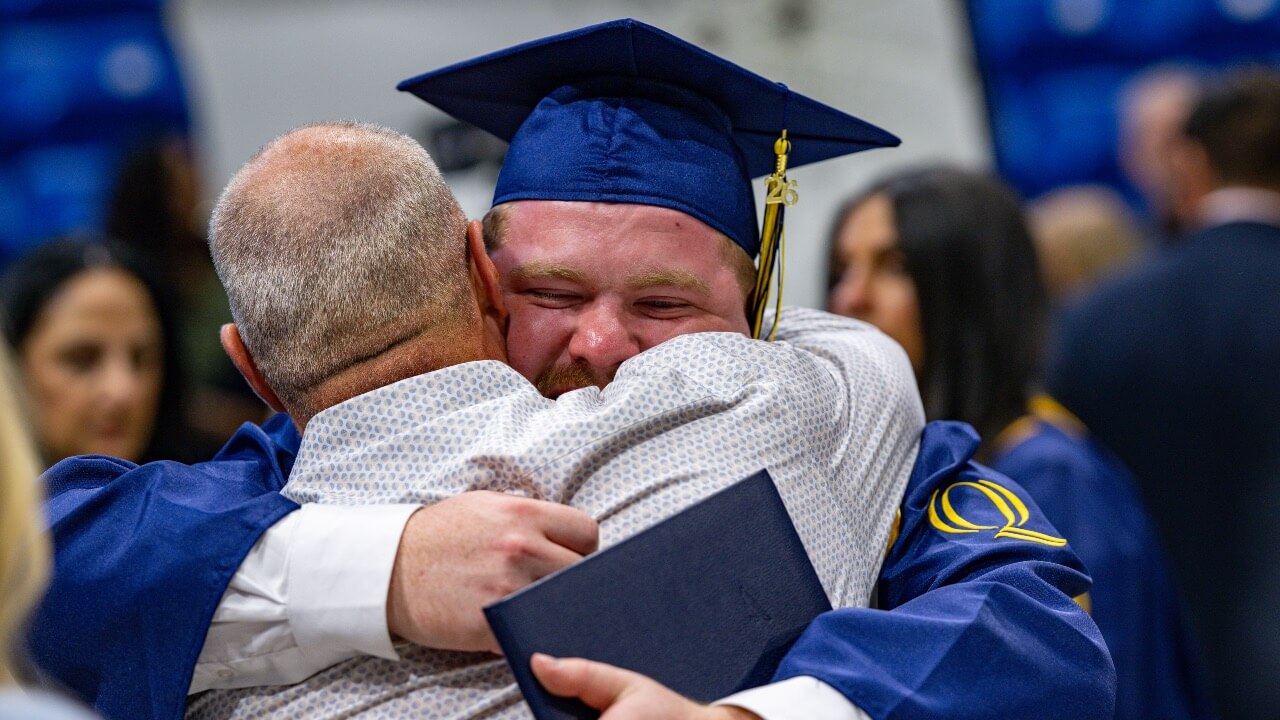 Graduate hugs loved one with diploma in hand