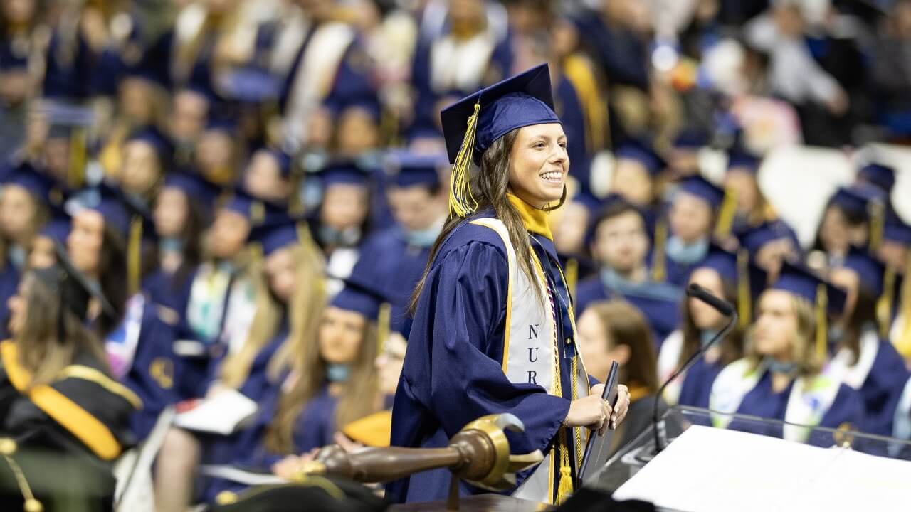 Graduate smiling and looking to their left while holding their diploma
