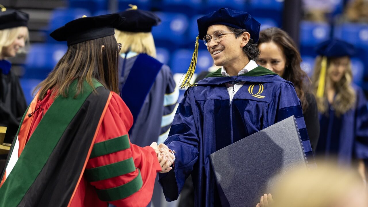 Graduate shakes hand with faculty member in cap and gown.