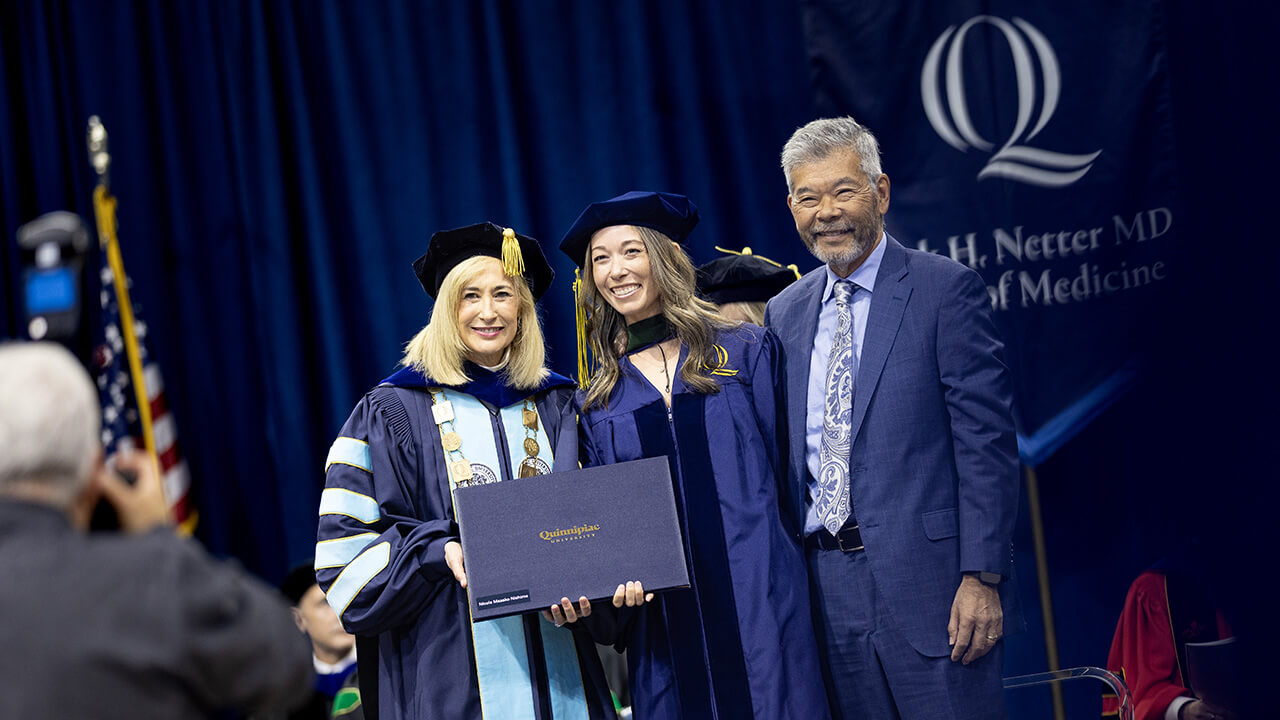 Graduate and guest pose with President Marie Hardin after being hooded