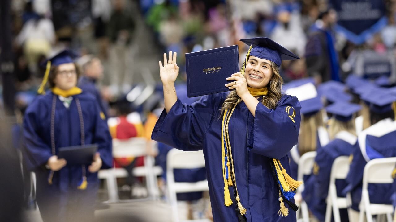 Graduate holds diploma while waving to the crowd with excitment