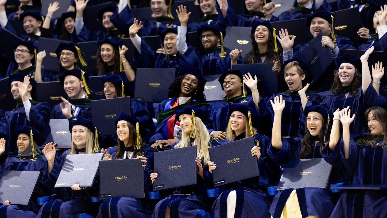 Graduates smile and cheer as they hold up their diplomas