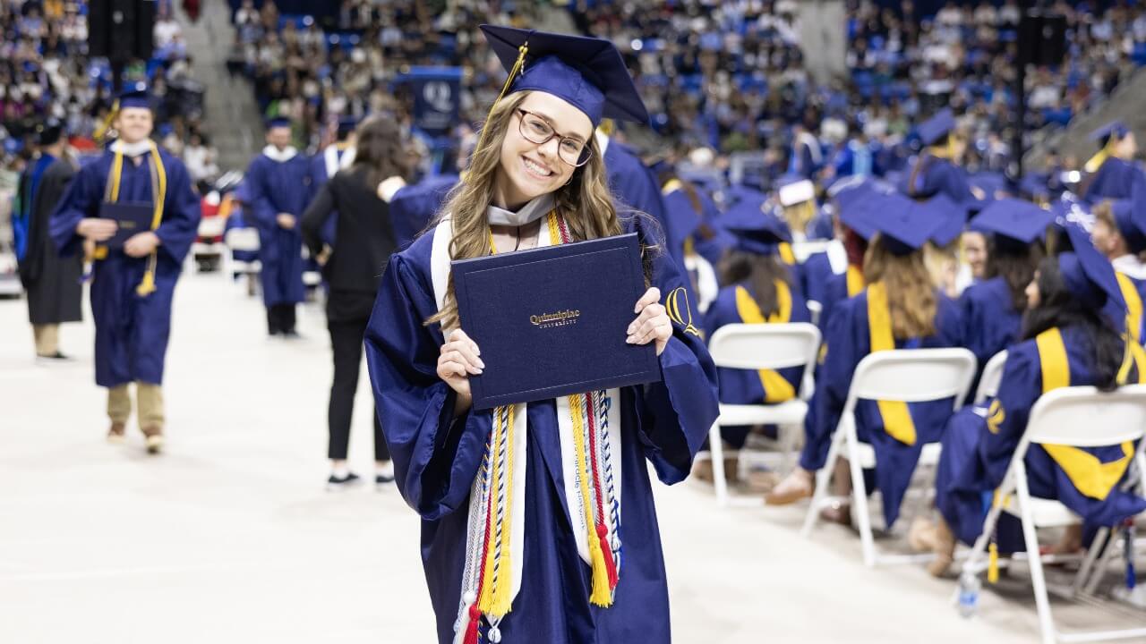 Graduate in cap and gown smiles with their diploma.