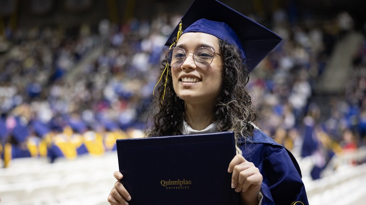 Graduate in cap and gown smiles with their diploma.