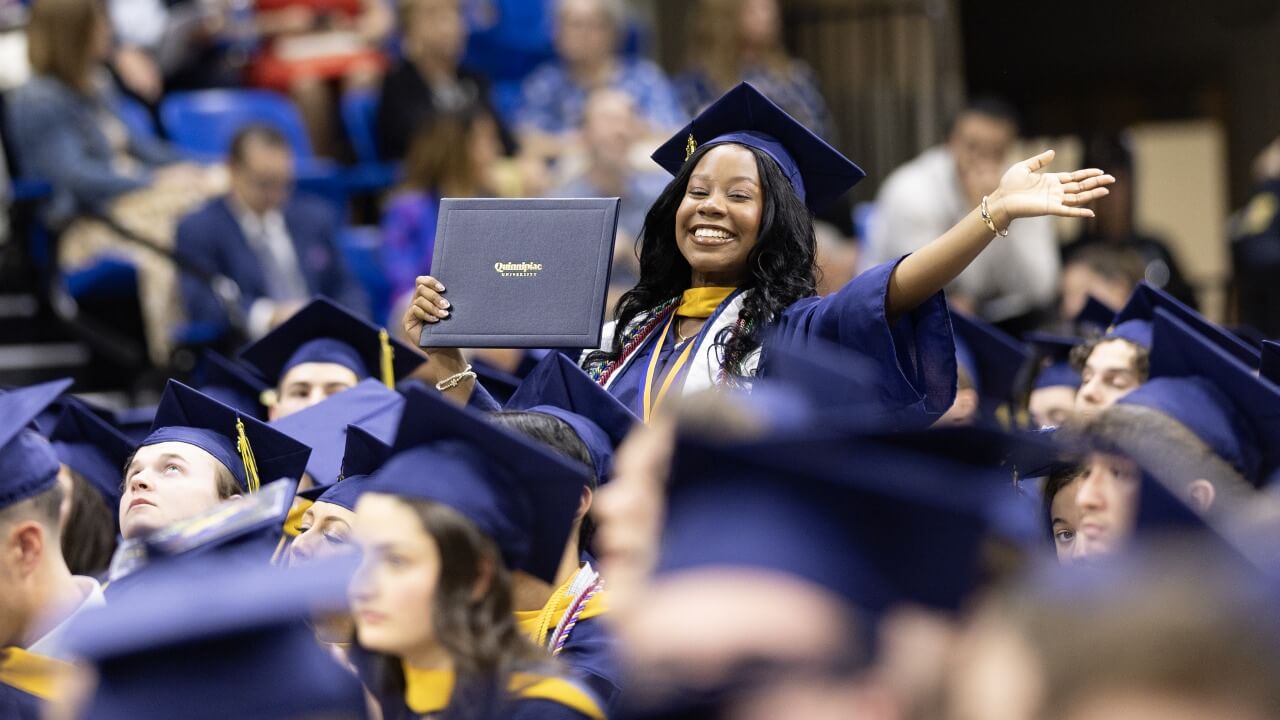 Graduate stands up with diploma and a smile in the audience
