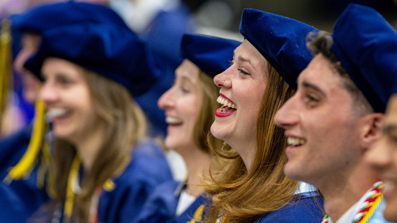 Graduates sit next to each other during ceremony and smile for a close up