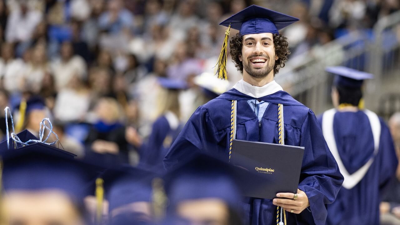 Graduate in cap and gown smiles with their diploma.