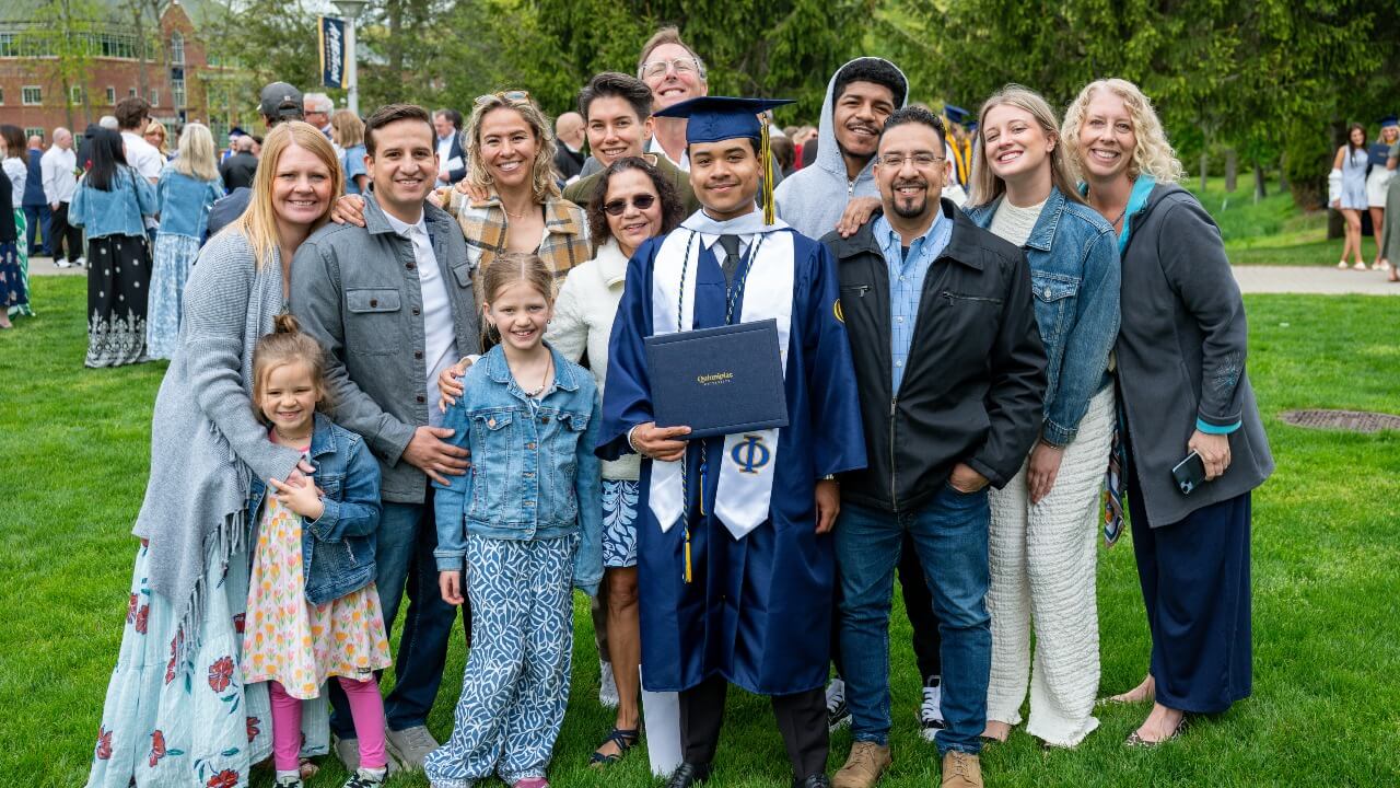 Graduate in cap and gown poses with their loved ones holding their diploma.