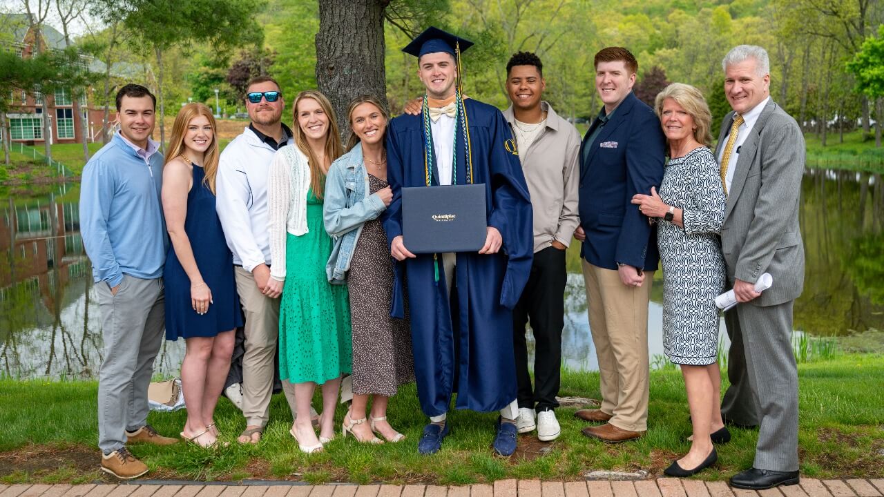 Graduate in cap and gown poses with their loved ones holding their diploma.